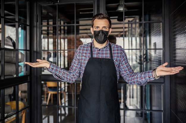 Instalação de catering e vírus corona. Um garçom uniformizado e com máscara protetora fica em frente à entrada do restaurante e proíbe a entrada sem proteção antivírus. Trabalhador de restaurante