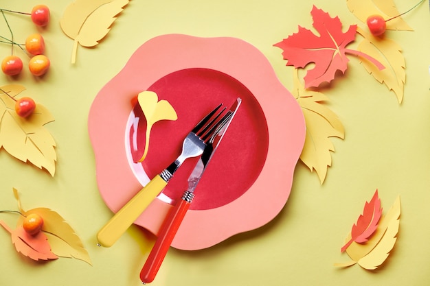 Instalação de mesa para a celebração do outono. Prato de plástico brilhante em papel amarelo com folhas de outono de papel