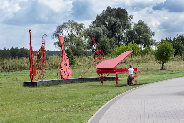 Instalação de orquestra em parque, piano vermelho, violoncelo e violino. mulher imita tocar piano. imagem abstrata no fundo da natureza.