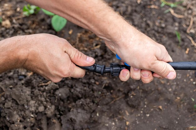 Foto instalação de um sistema de irrigação por gotejamento para o jardim um homem conecta o reforço de um tubo de hdpe