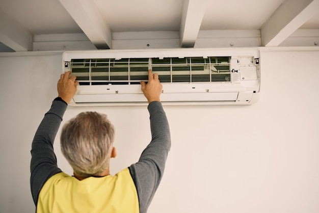 Instalación de construcción y parte posterior de un hombre con mantenimiento de aire acondicionado y reparación de CA Servicio de construcción y un manitas colocando una herramienta en una pared de una casa para mejorar y calentar el hogar