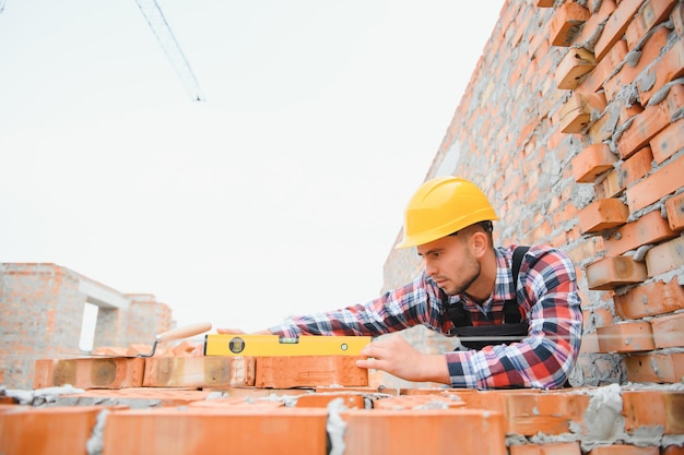 Instalación de pared de ladrillo Trabajador de la construcción en uniforme y equipo de seguridad tiene trabajo en la construcción