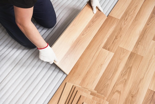 Foto instalación de piso laminado, detalle de manos de hombre sosteniendo baldosas de madera, sobre capa base de espuma blanca