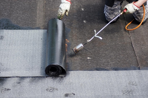 Instalación de techo plano con soplete de propano durante las obras de construcción con fieltro para techos