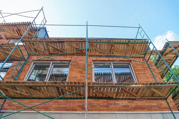 Se instalan andamios a lo largo de la pared del edificio en construcción Encrustado y pintura de la fachada de la casa Soportes metálicos y plataformas de madera para trabajar en altura