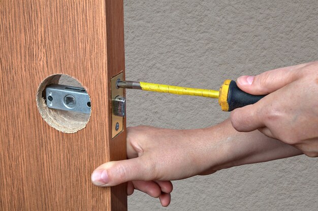 Foto instalando a maçaneta da porta com trava nas portas internas, close-up mãos do instalador com chave de fenda.