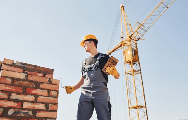 Instalando a parede de tijolos Trabalhador da construção em uniforme e equipamento de segurança tem trabalho na construção