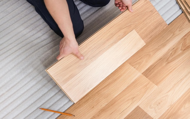 Instalando o piso laminado, vista detalhada de cima nas mãos do homem segurando a telha de madeira, encaixando-a, sobre a camada de base de espuma branca