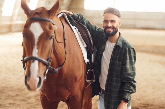 Foto instalando la silla de montar un joven con un caballo está en el hangar