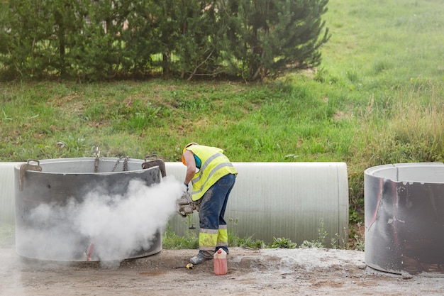 Instalando um tubo de concreto no solo para coletar água da chuva, o trabalhador faz buracos no concreto