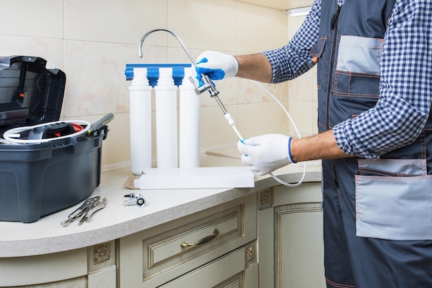 Instalar el filtro de purificación de agua Manos de fontanero con guantes reemplazan los cartuchos de filtro de agua en la cocina del hogar