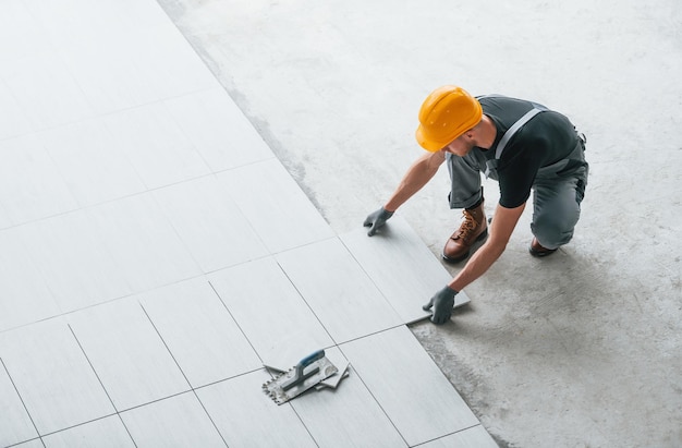 Installation von Platten Mann in grauer Uniform und orangefarbenem Schutzhelm arbeitet tagsüber in modernen großen Büros