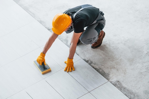 Installation von Platten Mann in grauer Uniform und orangefarbenem Schutzhelm arbeitet tagsüber in modernen großen Büros