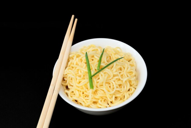 Instant chinesische lockige Nudeln in weißer Schüssel mit Holzstäbchen auf schwarzem Hintergrund Selektiver Fokus Asiatisches Lebensmittelkonzept Ungesunde Ernährung