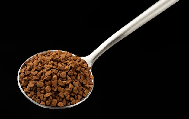 Instant-Granulatkaffee im Löffel auf schwarzem Hintergrund, Ansicht von oben