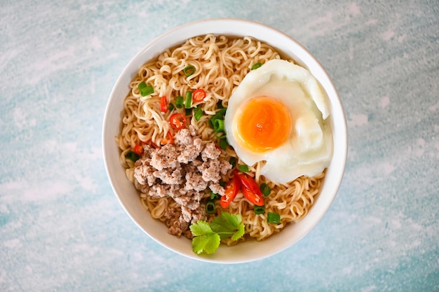 Instantnudeln kochen leckeres essen mit schüssel nudelsuppe nudeln schüssel mit gekochtem ei gehacktes schweinefleisch gemüse frühlingszwiebel zitrone limette salat sellerie und chili auf tisch essen