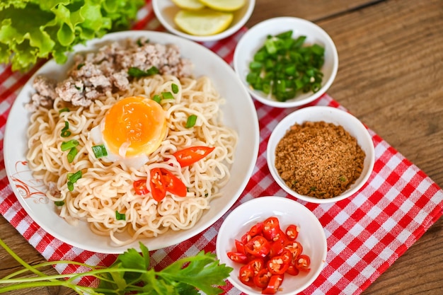 Instantnudeln kochen leckeres essen mit schüssel nudelsuppe nudeln schüssel mit gekochtem ei gehacktes schweinefleisch gemüse frühlingszwiebel zitrone limette salat sellerie und chili auf tisch essen