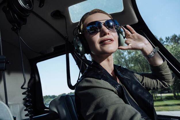 Instrucciones cruciales. Hermosa joven piloto sentado en una cabina de helicóptero y escuchando las instrucciones de los controladores de tráfico aéreo