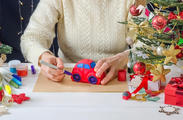 Instruções de fotos passo a passo para decoração de Natal uma garota pinta uma máquina de gesso passo 5 colorindo as rodas com uma caneta hidrográfica