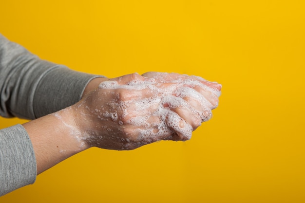 Instruções para lavar cuidadosamente as mãos e as unhas em um fundo amarelo. Mãos femininas em uma solução de sabão em um close-up de fundo brilhante.