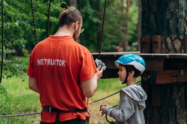 El instructor le dice al niño del casco de seguridad cómo usar la cuerda correctamente. Instrucción antes de pasar obstáculos