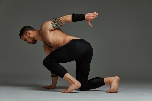Instructor de fitness instinto animal deportista mostrando su increíble flexibilidad con un movimiento de flujo animal en estudio sobre un fondo gris