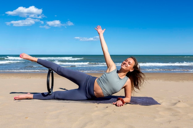 Instructor de fitness joven con un anillo de pilates cerca del mar concepto de rutina de yoga de fitness femenino