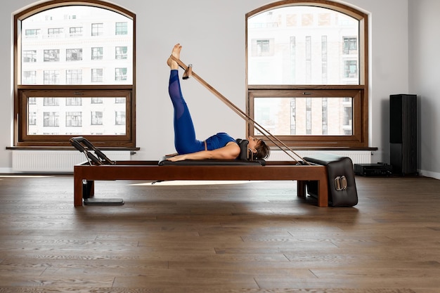 Foto el instructor hace ejercicios en el reformador una hermosa chica entrena en el moderno simulador reformador para ejercitar los músculos profundos el equipo reformador modernizado para pilates y yoga