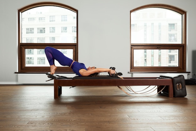 Foto el instructor hace ejercicios en el reformador una hermosa chica entrena en el moderno simulador reformador para ejercitar los músculos profundos el equipo reformador modernizado para pilates y yoga