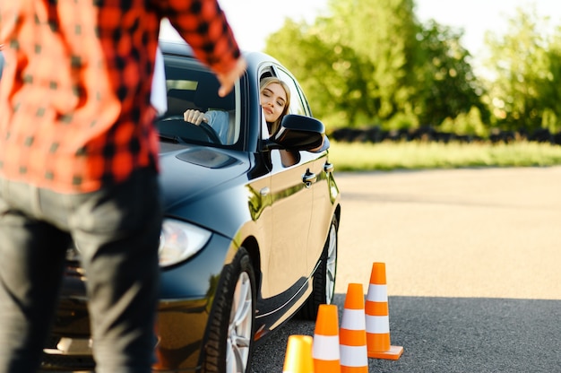 Foto instructor masculino y mujer en coche, conos de tráfico, lección de autoescuela. hombre enseñando a la señora a conducir un vehículo. educación sobre licencias de conducir