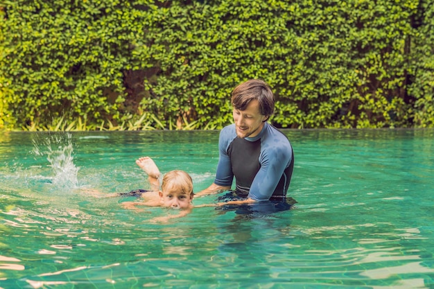 Instructor masculino de natación para niños enseña a un niño feliz a nadar en la piscina.