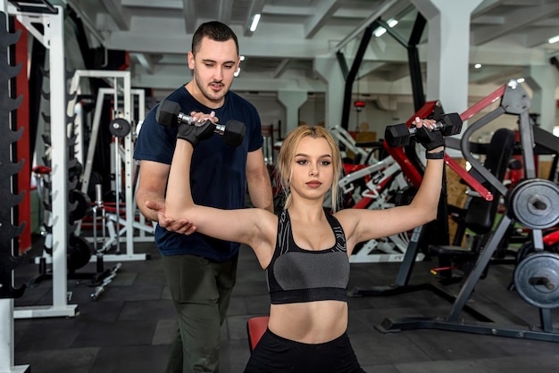 Instructor masculino personal que ayuda a la mujer a hacer ejercicio con pesas pesadas Entrenamiento del concepto de energía