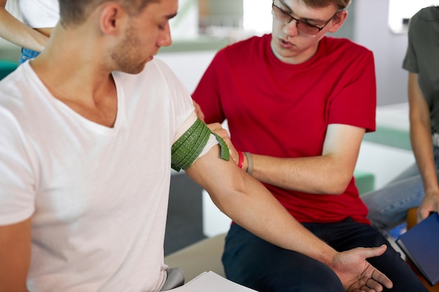 Foto instructor masculino profesional que usa torniquete para prevenir el sangrado durante el entrenamiento de primeros auxilios