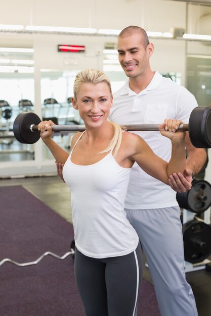 Foto instructor masculino que ayuda a la mujer con la barra de elevación en el gimnasio