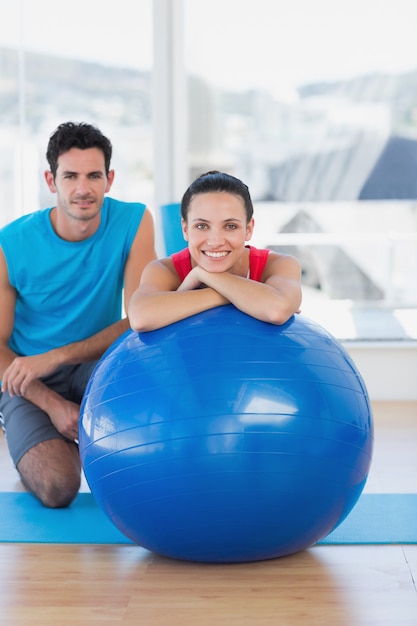 Instructor y mujer sonriente con balón de ejercicio en el gimnasio