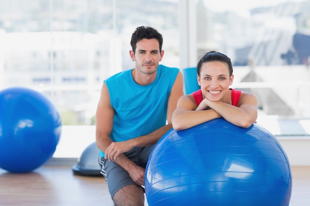 Instructor y mujer sonriente con balón de ejercicio en el gimnasio