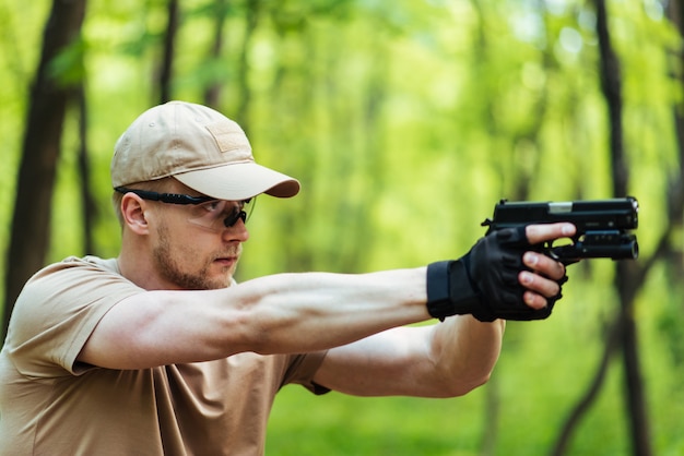 Instructor con pistola en bosque conduce apuntando y posando en la cámara