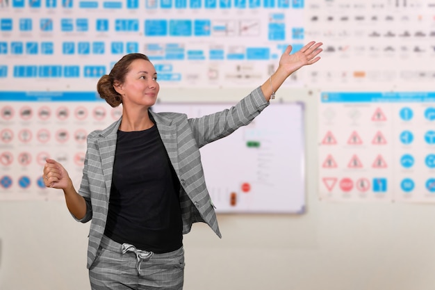 Instructora de conducción mujer enseña teoría sobre fondo borroso de la sala de formación con imágenes de señales de tráfico