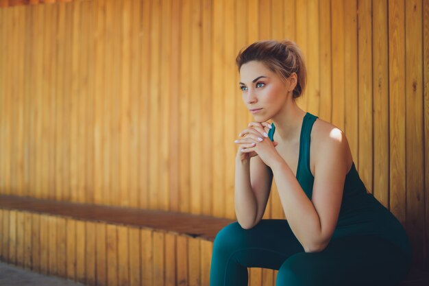 Instructora de fitness joven hermosa da lecciones de video usando la computadora portátil en una terraza de madera en la calle.