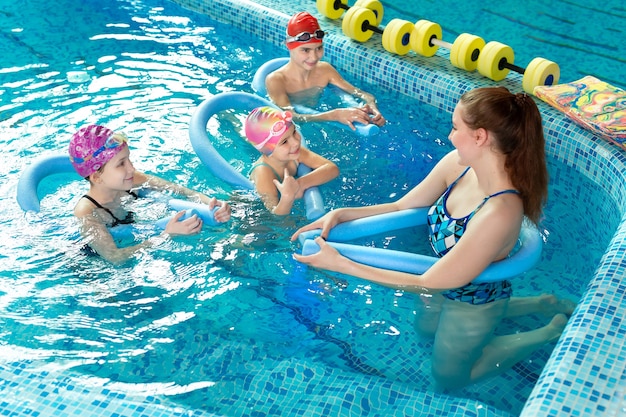Instructora joven enseña a los niños a nadar en la piscina.