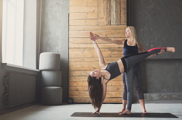 Instructora de yoga y mujer joven en tabla lateral en clase de estiramiento, ejercicio vasisthasana. Colocar yoga chica equilibrio sobre la estera en el interior en el gimnasio fitness studio