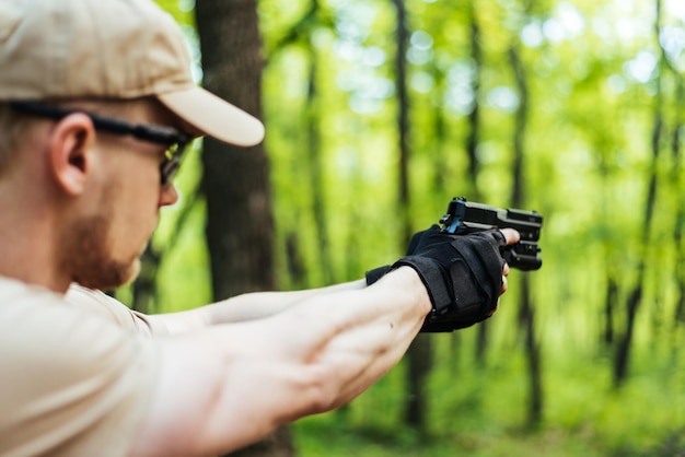 Instruktor mit Waffe im Wald führt, zielt und posiert vor der Kamera