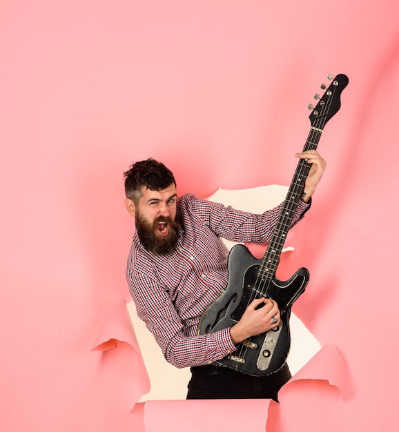 Foto instrumento musical tocar guitarra baixo elétrico guitarra guitarrista através de um buraco no papel rosa segura a guitarra