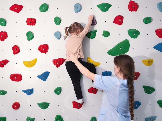 instrutor de fisioterapeuta ajudando a menina a escalar a parede no ginásio. integração sensorial