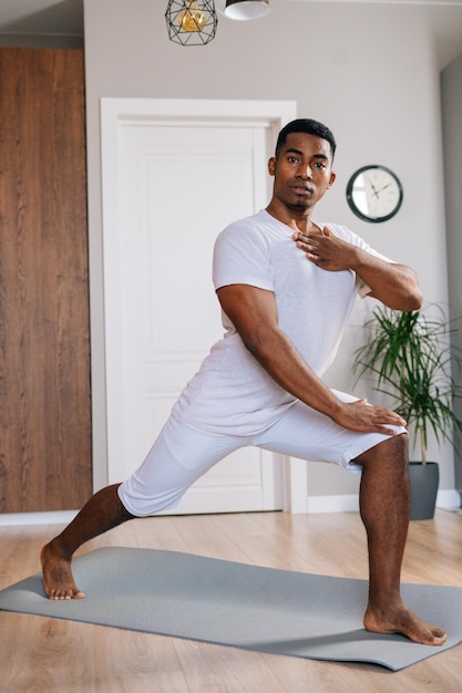 Instrutor de fitness afro-americano bem sucedido fazendo exercício esportivo em pé no tapete de ioga