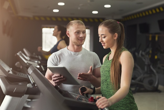 Instrutor de fitness ajuda jovem no aparelho elíptico. Treino cardiovascular na academia, estilo de vida saudável, espaço de cópia