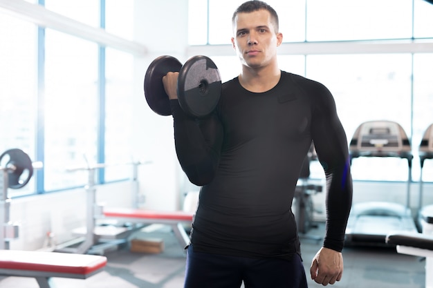 Instrutor de fitness bonito posando com halteres no ginásio