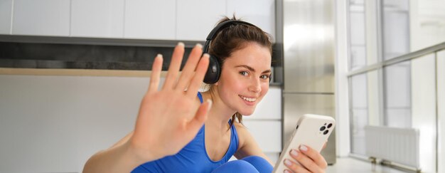 Instrutor de fitness feliz em casa faz exercícios com fones de ouvido e smartphone ouve música e