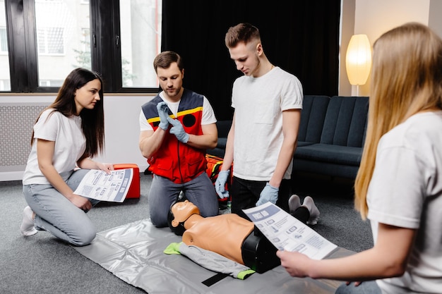 Instrutor de jovem ajudando a fazer compressões cardíacas de primeiros socorros com manequim durante o treinamento em grupo dentro de casa