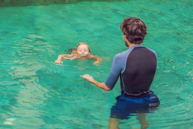 Instrutor de natação para crianças ensina um menino feliz a nadar na piscina.